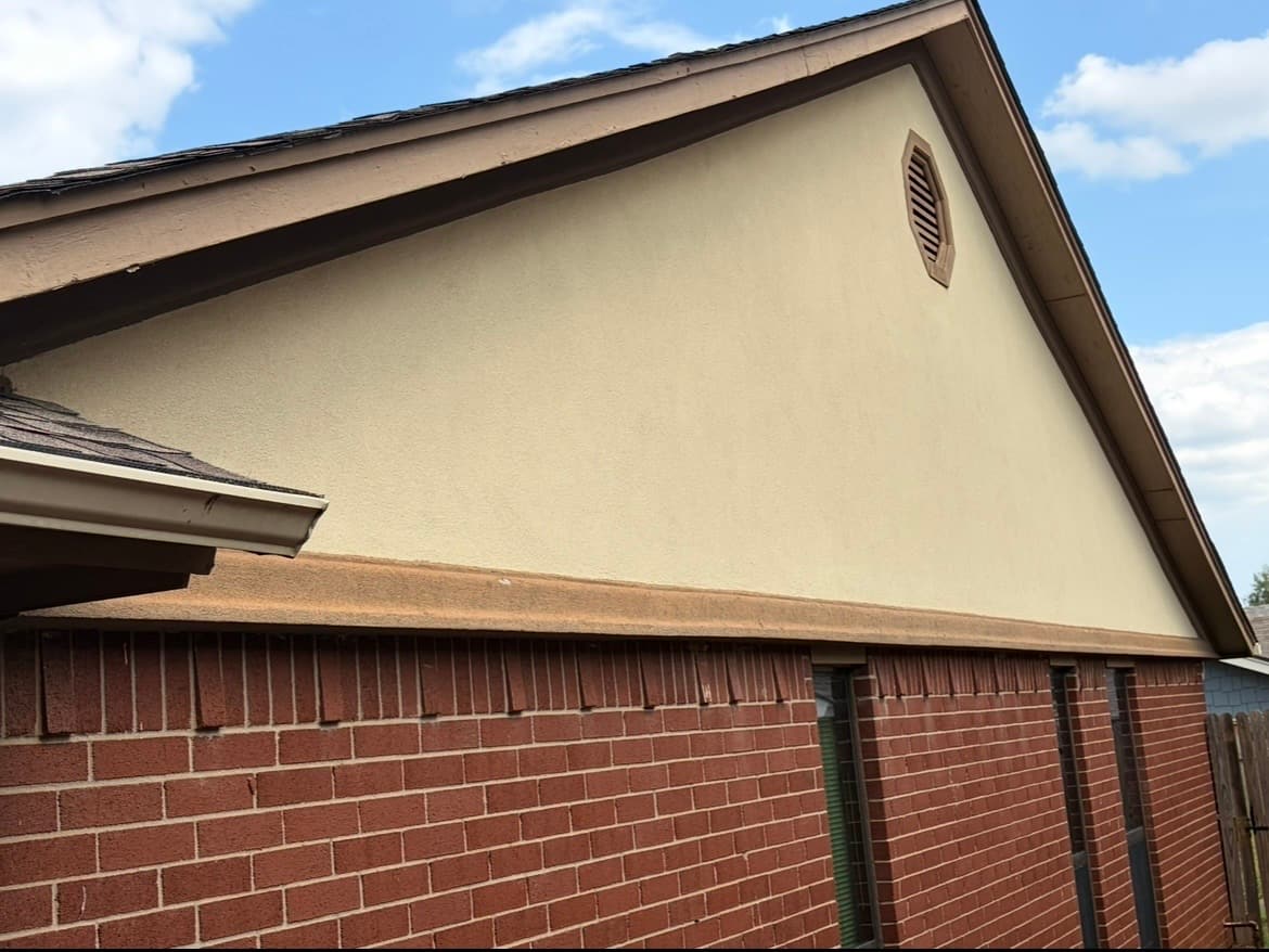 Stucco gable finished above red brick with a round gable vent