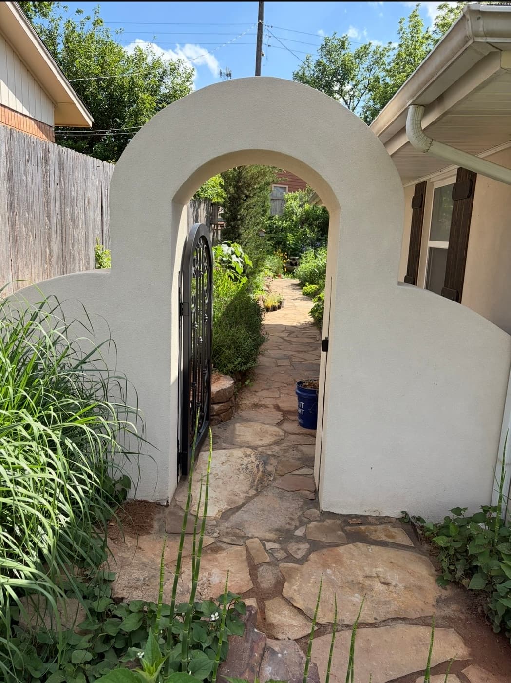 White stucco garden wall with an arched top and wrought iron gate