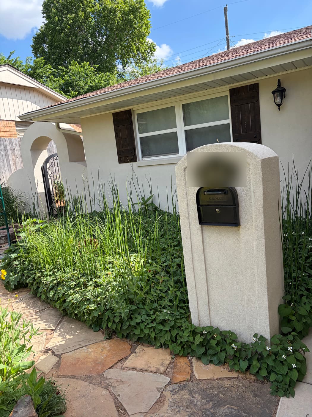 Cream stucco home with a matching stucco mailbox pillar and flagstone walkway