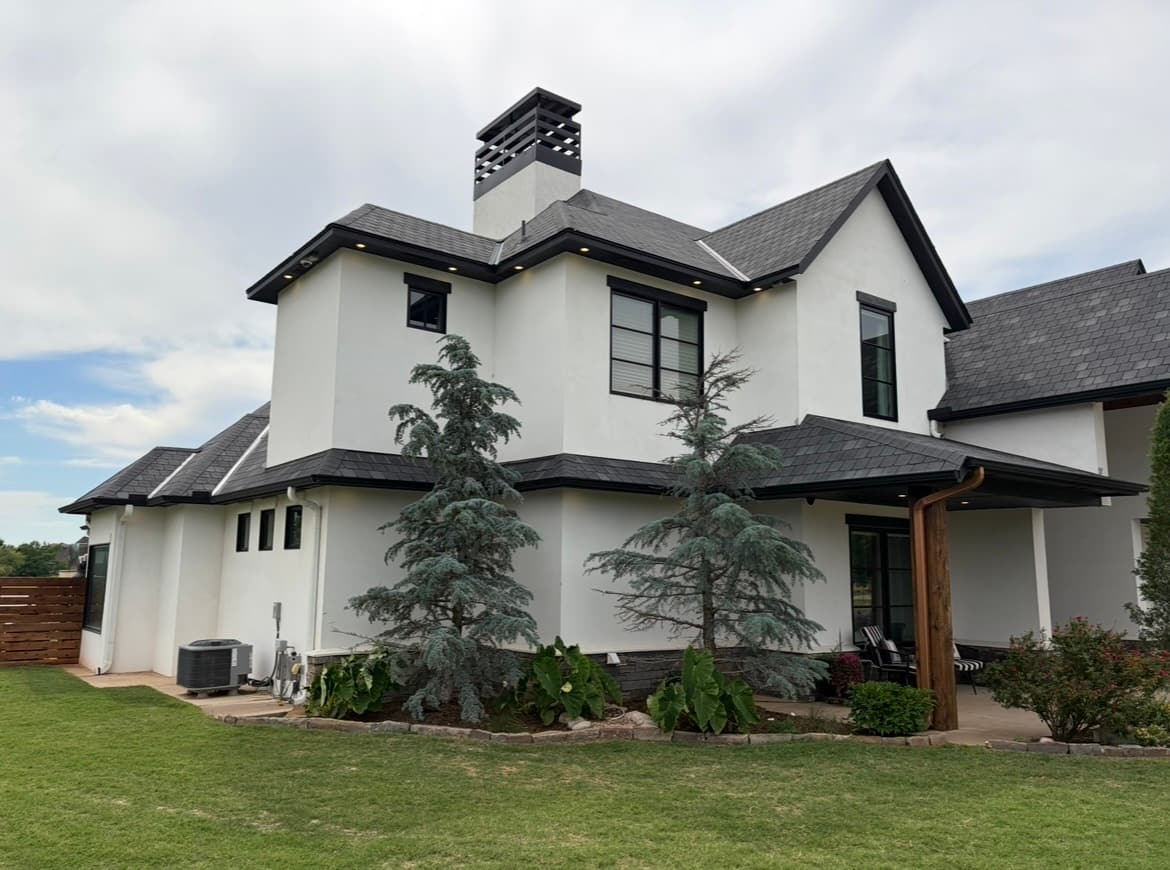 Two-story white stucco home with dark trim and a stucco chimney